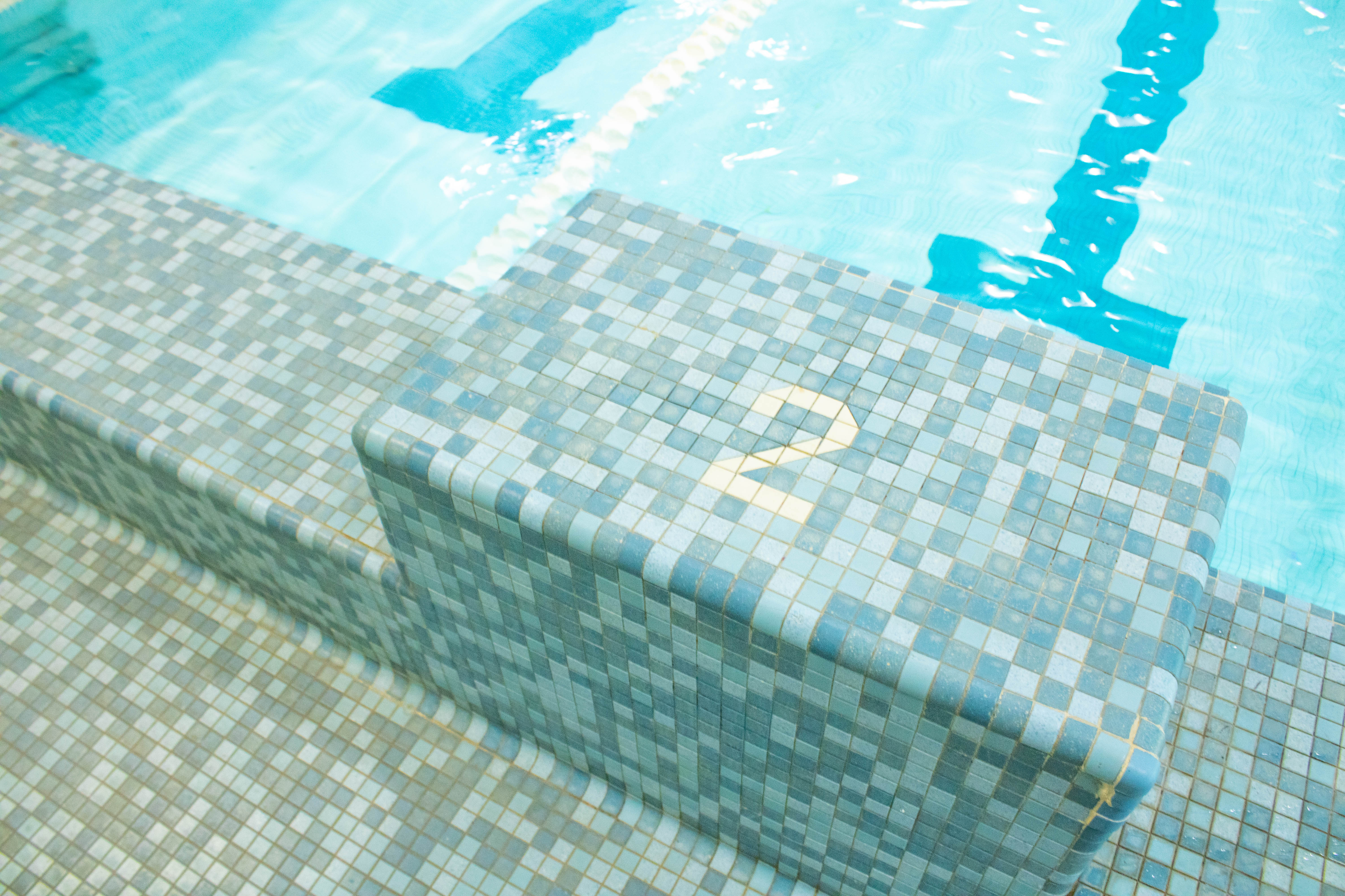 Image of a blue square tiled block with the number 2 in white tiles and a clear pool with the white colors of the lane line showing.