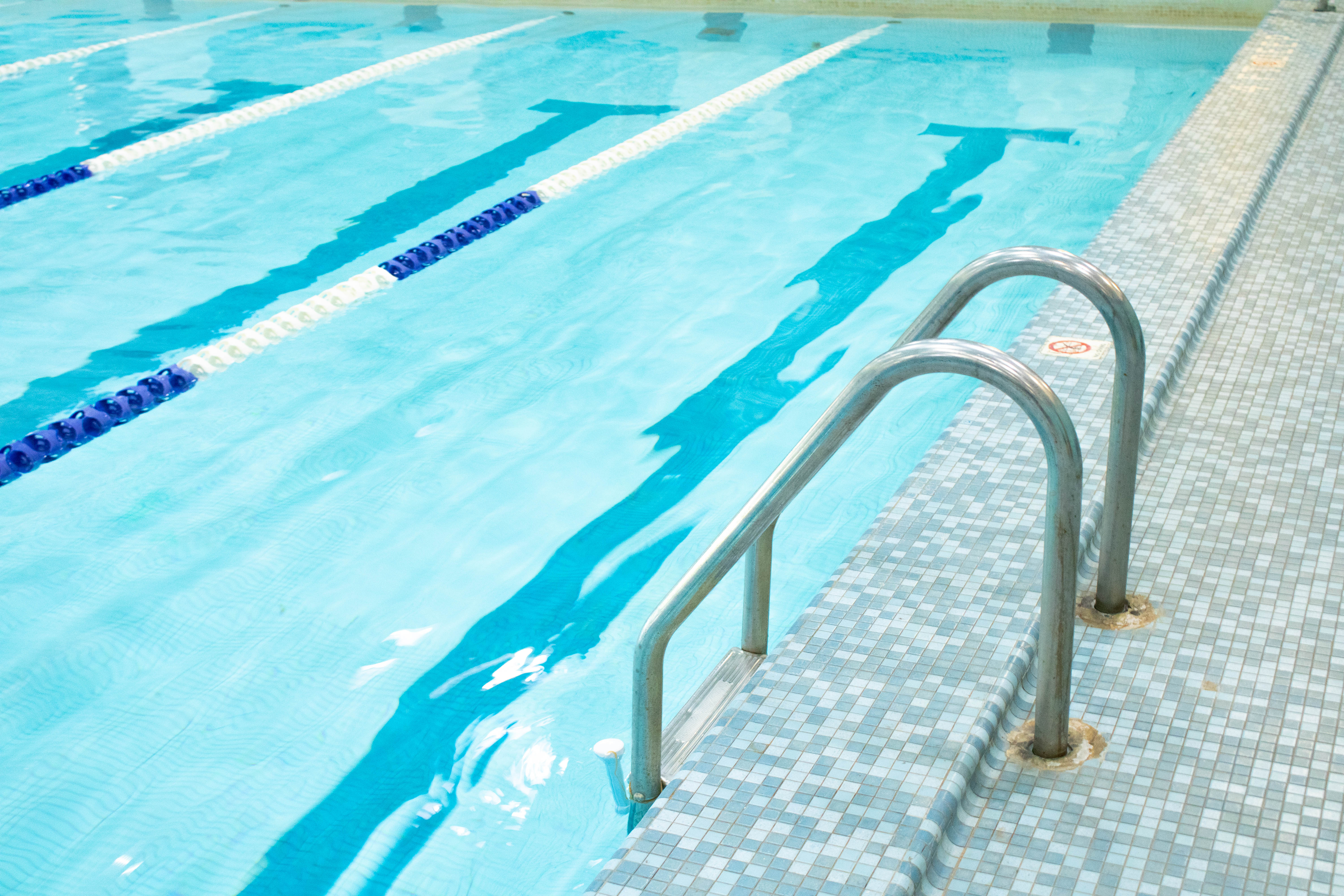 Image of a silver ladder surrounded by different colors of blue square tiling with a clear pool with two lane lines with royal blue and white colors.